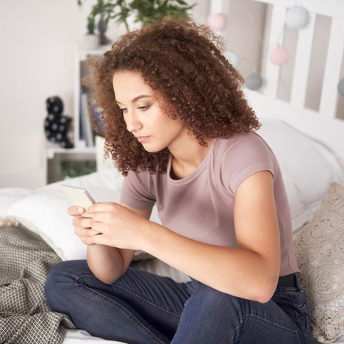 Young woman looking at her phone wondering how to tell her parents she is pregnant